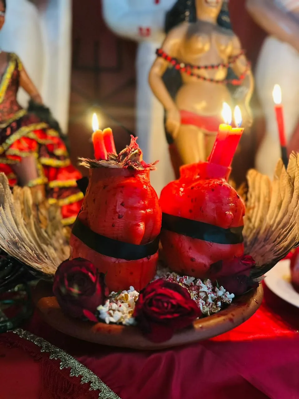 Altar de Pombagira com velas vermelhas acesas, rosas escuras, asas e imagens de entidade