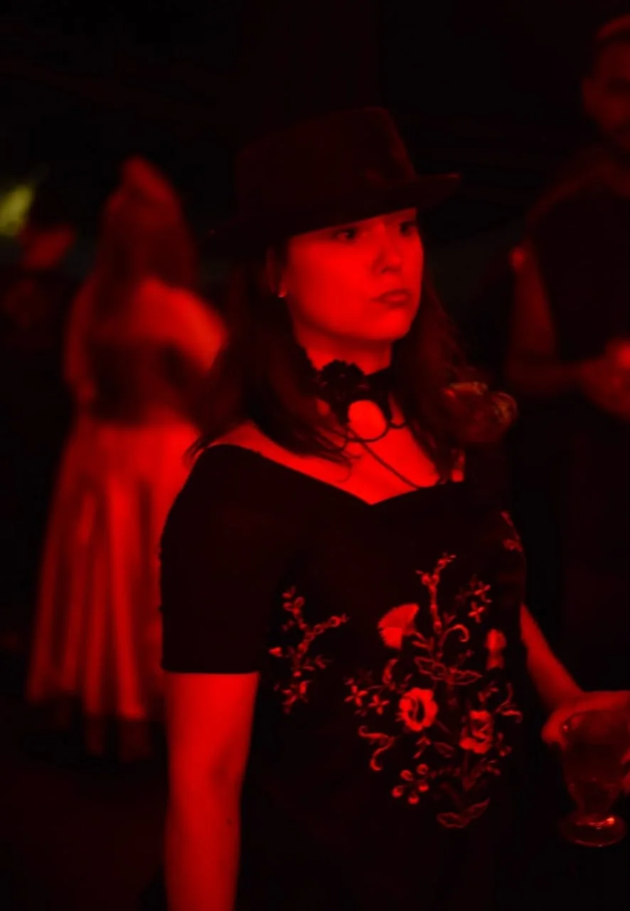 Paola da Farrapo de chapéu preto e vestido bordado, iluminada por luz vermelha durante a gira