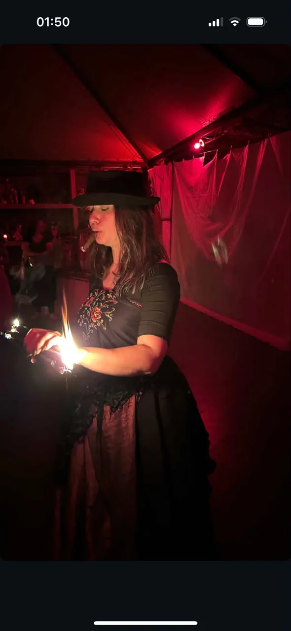 Paola da Farrapo acendendo fogo sobre o altar, sob luz vermelha, de chapéu preto